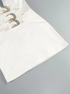 Close-up of white halter dress with rhinestone horseshoe buckles and cut-out details