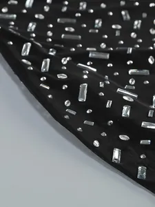 Close-up detail of sparkling rhinestone embellishments on black mesh evening dress fabric.
