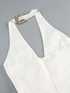 Detailed view of white halter-neck dress featuring a glamorous gold rhinestone buckle.