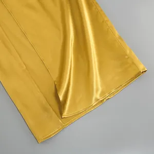 Detail of gold satin maxi dress showing the side split and smooth fabric texture
