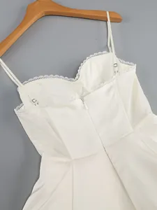 Close-up of white spaghetti strap dress with lace trim and mesh panels for elegant look.