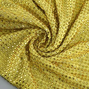 Detaillierte Ansicht funkelnder goldener Strasssteine auf gelbem Netzstoffkleid.