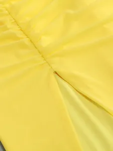 Macro detail of a bright yellow ruched evening dress showing the high slit and mesh texture.