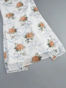 Gros plan sur l'élégant imprimé rose et ruban sur l'ourlet fendu d'une robe fleurie blanche.