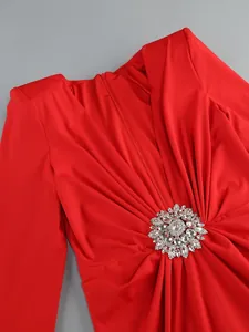 Close-up detail of a red pleated long sleeve dress featuring a crystal flower ornament