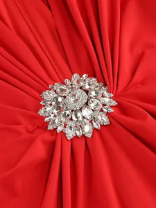 Close-up detail of a red pleated evening dress featuring a large crystal rhinestone brooch.