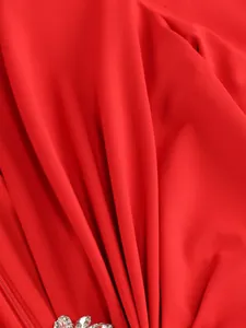 Macro detail of red elegant dress featuring luxurious pleated fabric and crystal accents.