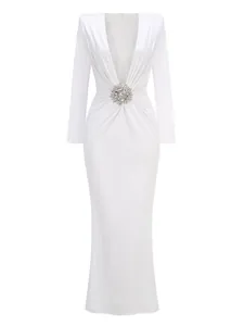 Detail view of an elegant white long sleeve evening gown featuring a sparkling crystal brooch.