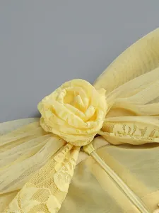 Close-up of a yellow mesh evening dress featuring an elegant lace flower detail and zipper.