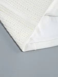Detailopname van witte avondjurk met elegante parelborduursels op gladde stofafwerking