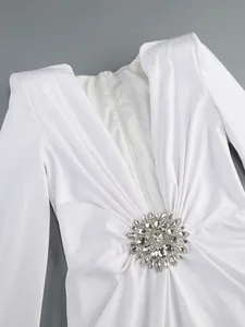 Close-up detail of white long sleeve dress with deep V-neck and crystal flower ornament