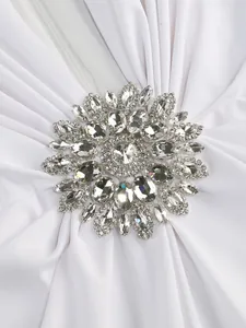 Detailed close-up showing the crystal rhinestone brooch on a white ruched evening party dress