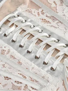 Close-up of white lace dress featuring elegant satin ribbon corset lacing detail.