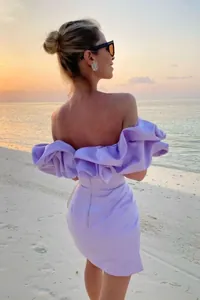Vista trasera de modelo con vestido lila con volantes y hombros descubiertos en playa