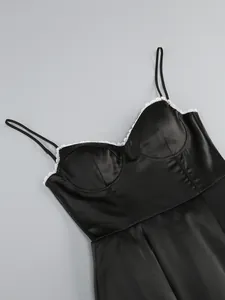 Detail shot of black satin camisole dress with delicate white lace trim on neckline.