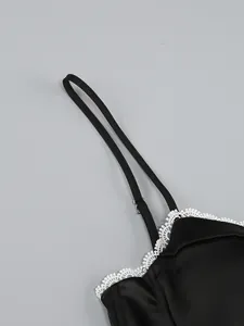 Detail shot of adjustable strap and white lace trim on a black satin camisole dress.