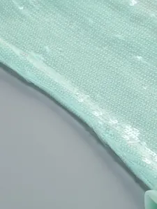 Macrodetail van glinsterende lovertjes op de muntgroene transparante mesh van een avondjurk