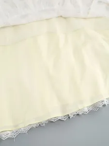 Detail of dress hem showing layers of yellow fabric, white lace trim, and fine mesh