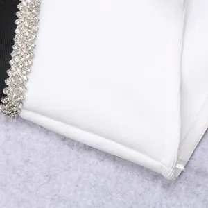 Macro detail of white bandage dress with black rhinestone trim and knit texture.