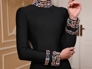 Close-up of colorful gemstone details on a black evening dress collar and sleeve cuffs.