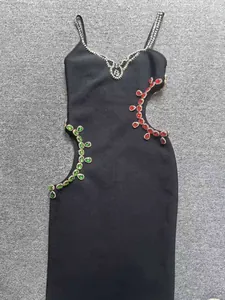 Detalle de vestido bandage negro con recortes asimétricos decorados con gemas rojas y verdes.