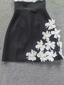 Détail rapproché de l'applique fleurie blanche 3D sur une mini robe bandage noire de soirée