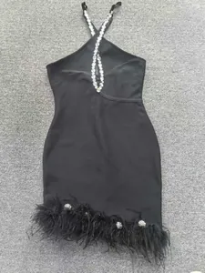 Détail d'une robe bandage noire avec bretelles en strass et bordure en plumes