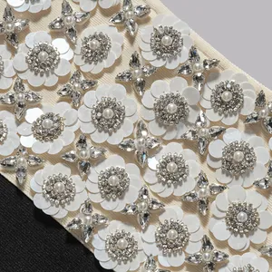 Detailaufnahme von eleganten Paillettenblumen und Perlen auf weißem Bandagenkleid.