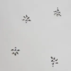 Gedetailleerde macro-opname van sprankelende zilveren strass-bloemmotieven op wit jurkenmateriaal