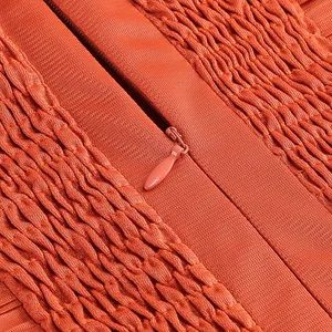 Primer plano de la cremallera invisible y textura fruncida en un vestido de gasa color naranja.