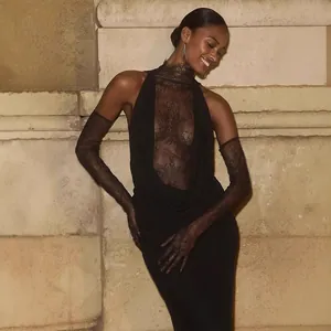 Model wearing a sexy black lace halter dress with matching gloves against a stone wall.