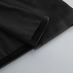 Close-up of smooth black fabric and precise stitching on the hem of a draped dress.