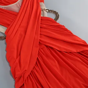 Detalle de un vestido largo rojo drapeado con cadenas doradas y textura plisada