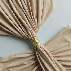 Detalle de un anillo dorado texturizado en un vestido largo beige sin mangas.
