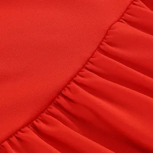 Primer plano de tela roja texturizada con detalles de volantes plisados en un vestido largo.