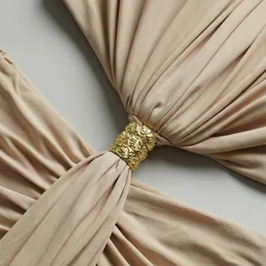Detalle de vestido beige con elegante nudo retorcido y herraje de anillo dorado.