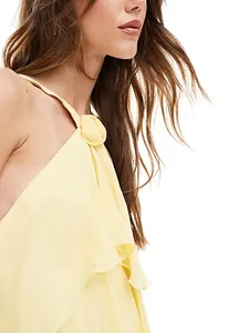 Primer plano de vestido amarillo con capas y detalle de flor 3D en el escote.