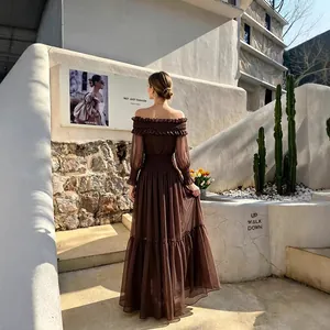 Vista trasera de mujer en vestido largo marrón con hombros descubiertos en el jardín