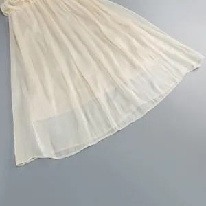 Close-up detail of the elegant pleated sheer hemline of this cream-colored evening dress