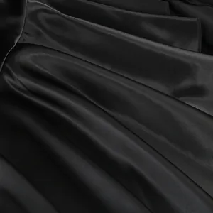 Primer plano de tela de satén negro brillante con elegantes detalles de volantes y textura.