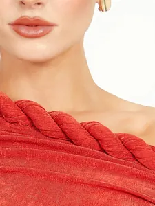 Detalle de vestido rojo de un hombro con tirante de cuerda trenzada y plisado fino