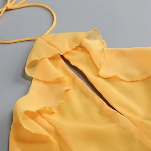 Primer plano de un vestido halter amarillo con bordes de volantes y tela de gasa texturizada.