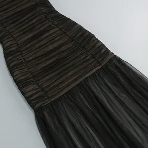 Detalle macro de un vestido palabra de honor de malla negra con elegantes pliegues fruncidos.