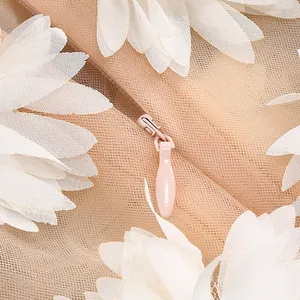 Detalle de encaje floral 3D blanco y cremallera oculta en un vestido de malla nude.
