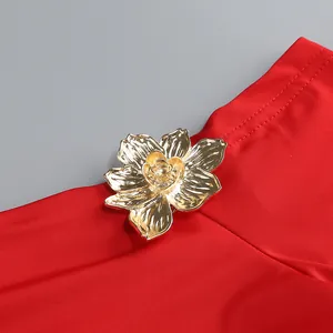 Detalle de un elegante adorno de flor dorada sobre tela de prenda roja vibrante.