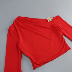 Detalle de elegante top rojo de un solo hombro con broche de flor dorada en 3D