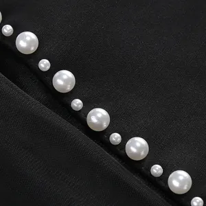 Detalle macro de perlas blancas cosidas a mano en tejido de malla negra y vestido bandage