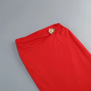Vista detallada de falda larga roja de talle alto con adorno de flor de metal dorado.