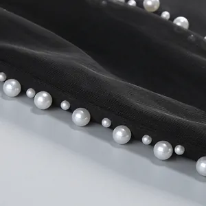 Primer plano de elegantes perlas blancas cosidas sobre malla negra de un vestido de gala