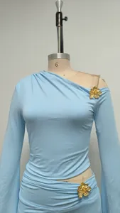 Detalle del top azul claro de un solo hombro con un elegante adorno de flor dorada en 3D.